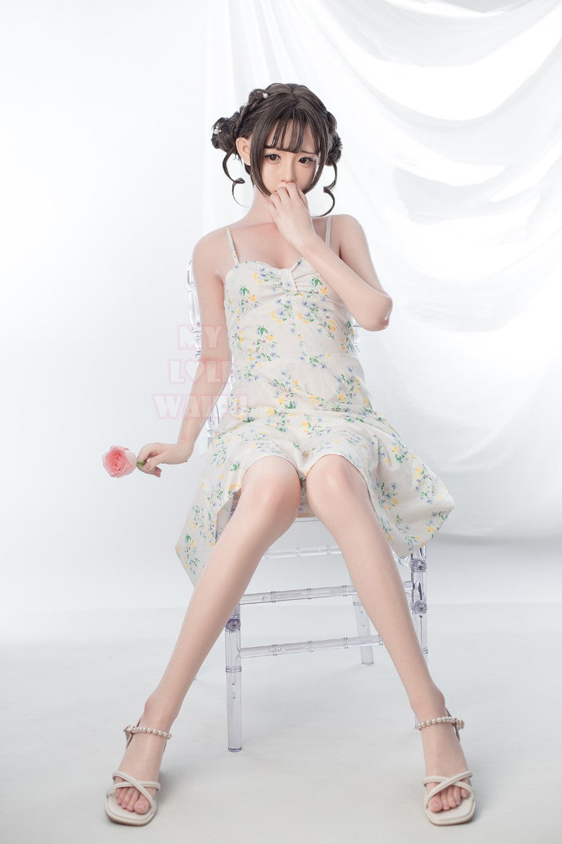 Nanami silikonsexdocka 150 cm, sitter i vit spetsklänning och visar sin kurviga kropp med B-kupa mot ljus studiobakgrund.